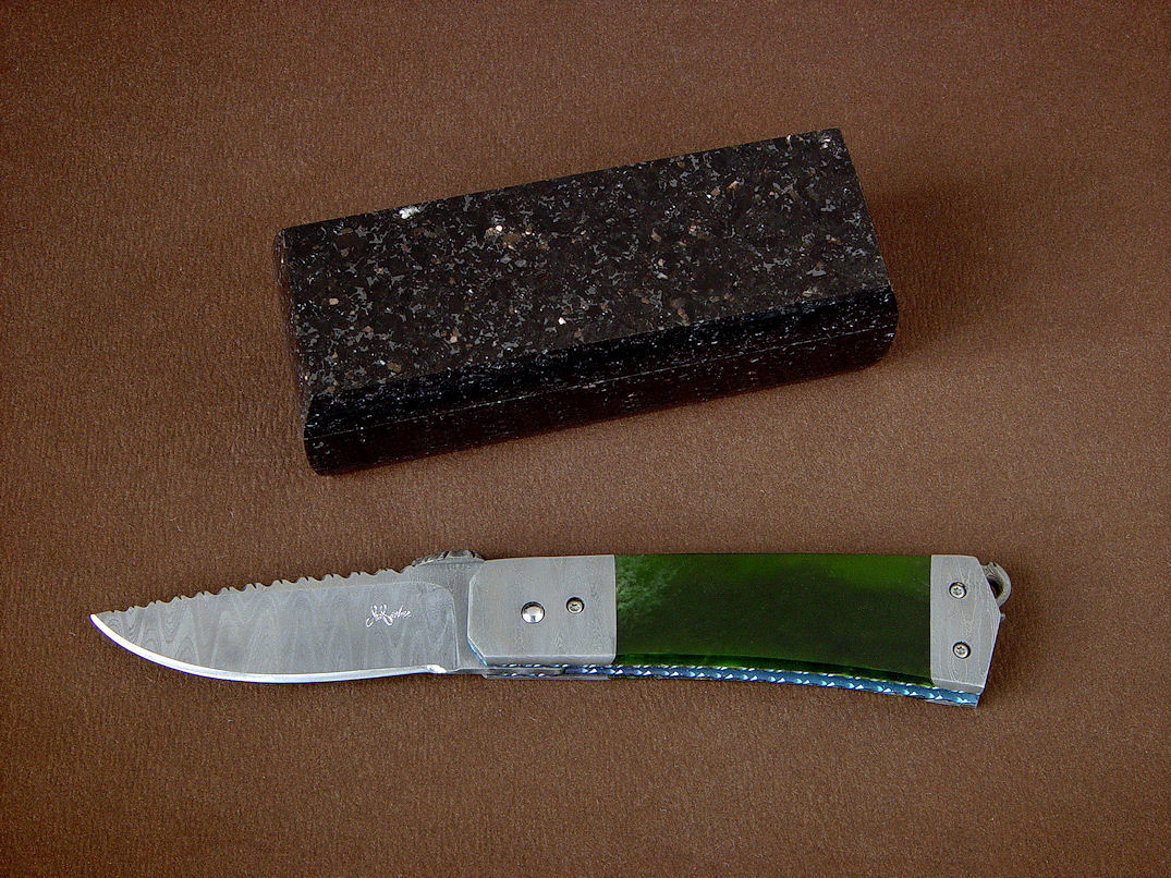 "Aries" folding knife, obverse side view in damascus stainless steel blade and bolsters, anodized titanium liners, New Zealand Jade gemstone handle, Black Galaxy Granite gemstone case