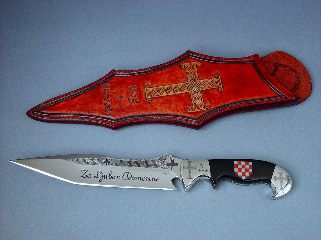 "Duhovni Ratnik" obverse side view. Knife in hand-engraved 440C high chromium stainless steel blade, hand-engraved 304 stainless steel bolsters, handle of Black Nephrite Jade gemstone inlaid with a mosaic of Red River Jasper and White Geodic Quartz. Sheath is hand-carved, hand-dyed leather shoulder