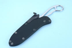 "Xanthid" tactical/working dive knife, sheathed view showing front face of sheath and cam-lock mechanism made of grayed and passivated 304 stainless steel and anodized titanium springplate. Camlock allows retention to clear serrations while being sheathed or unsheathed.