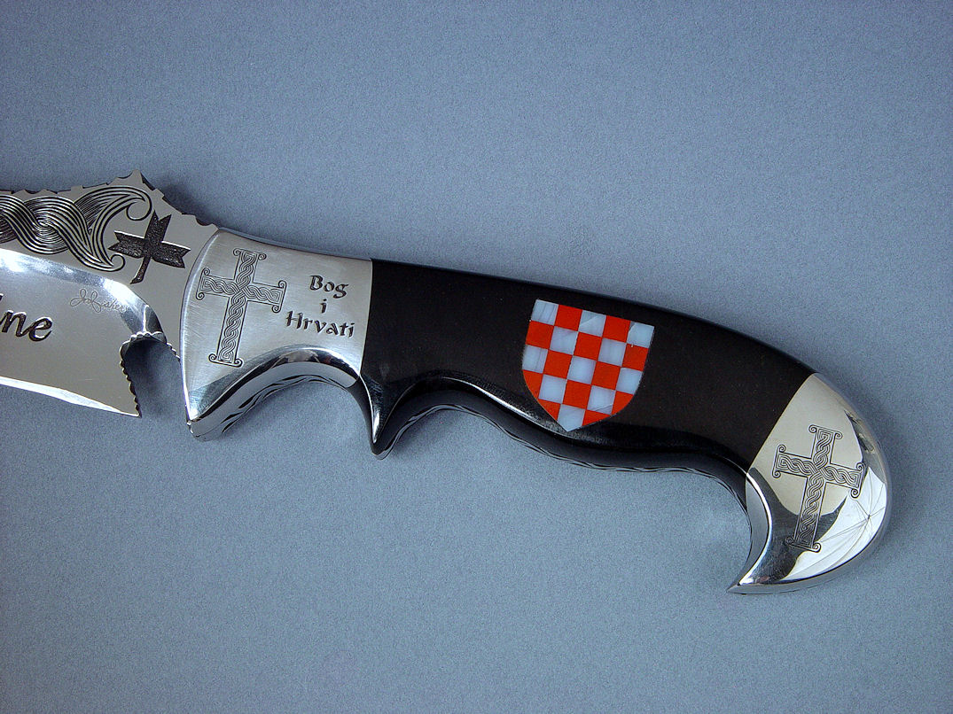 "Duhovni Ratnik" obverse side view. Knife in hand-engraved 440C high chromium stainless steel blade, hand-engraved 304 stainless steel bolsters, handle of Black Nephrite Jade gemstone inlaid with a mosaic of Red River Jasper and White Geodic Quartz. Sheath is hand-carved, hand-dyed leather shoulder