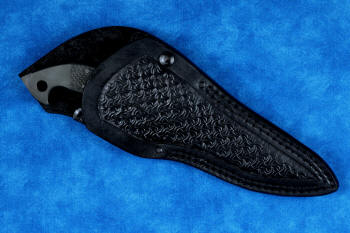 "Ari B'Lilah" counterterrorism, tactical, combat knife, sheathed view in T4 cryogenically treated 440C high chromium martensitic stainless steel blade, 304 stainless steel bolsters, carbon fiber handle, sheath in 9-10 oz. leather shoulder, basketweave stamp tooled, double row nylon stitching, stainess steel reinforcement and snaps, post locking secure
