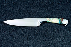 Obverse side view of "Cygnus" Custom handmade chef's knife in T3 cryogenically treated 440C high chromium stainless steel blade, 304 stainless steel bolsters, Cuprite mosaic gemstone handle, hand-tooled leather sheath